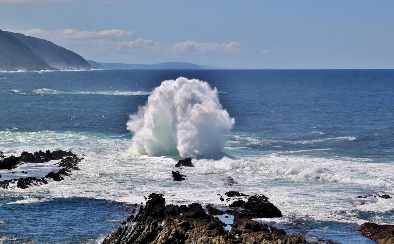 Heavy surf bursting white over dark rocks under a blue sky